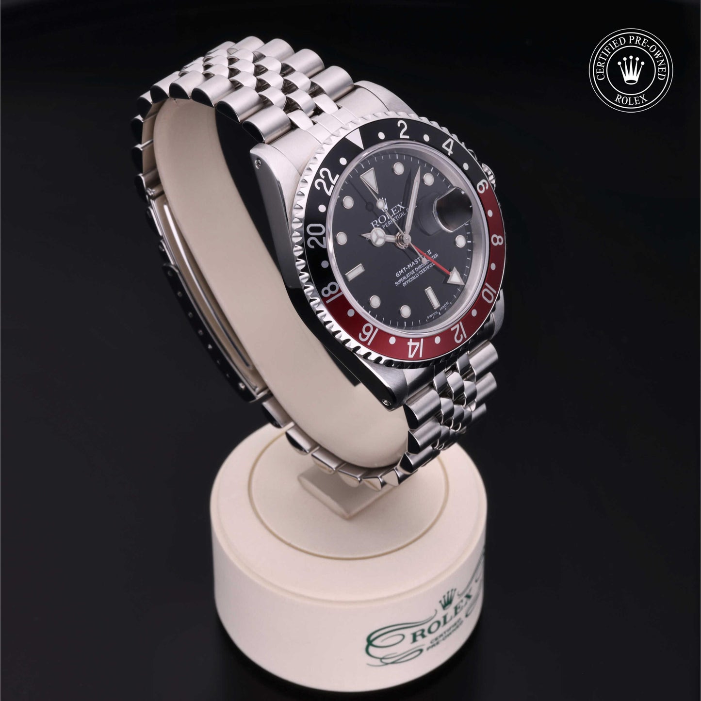 Rolex GMT-Master II with Jubilee bracelet, red and black bezel and black dial on a presentation stand against a black background.