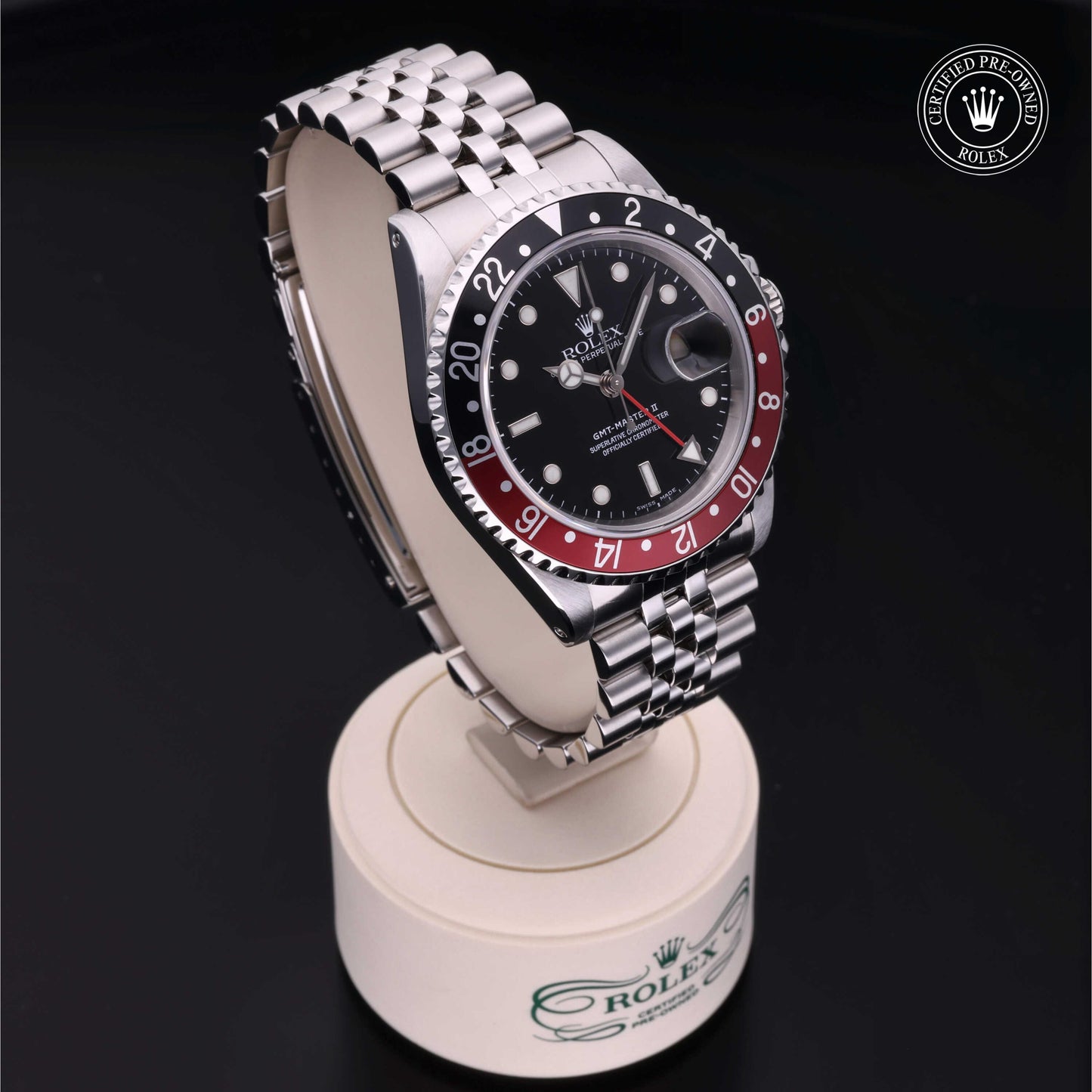 Rolex GMT-Master II with Jubilee bracelet, red and black bezel and black dial on a presentation stand against a black background.