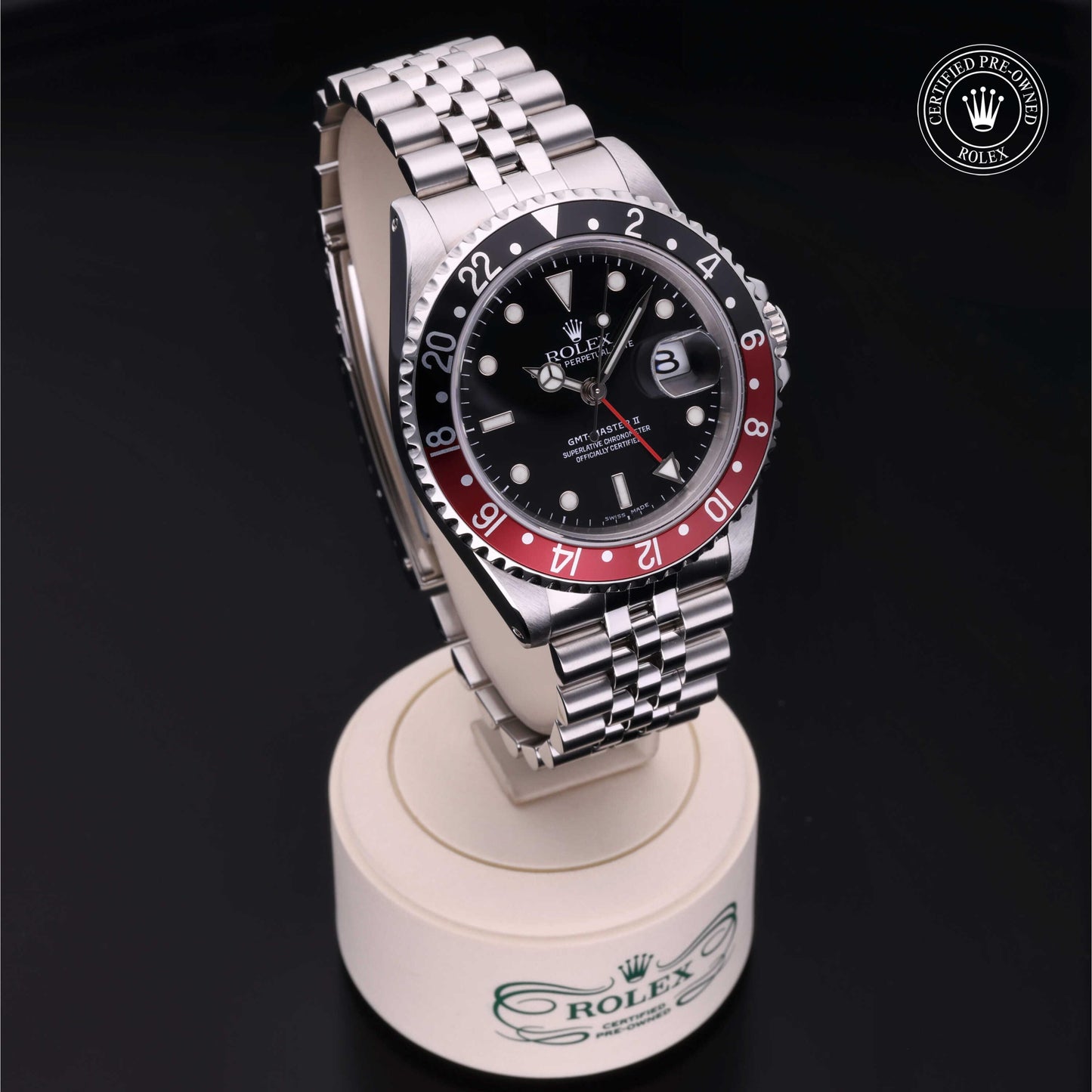 Rolex GMT-Master II with Jubilee bracelet, red and black bezel and black dial on a presentation stand against a black background.