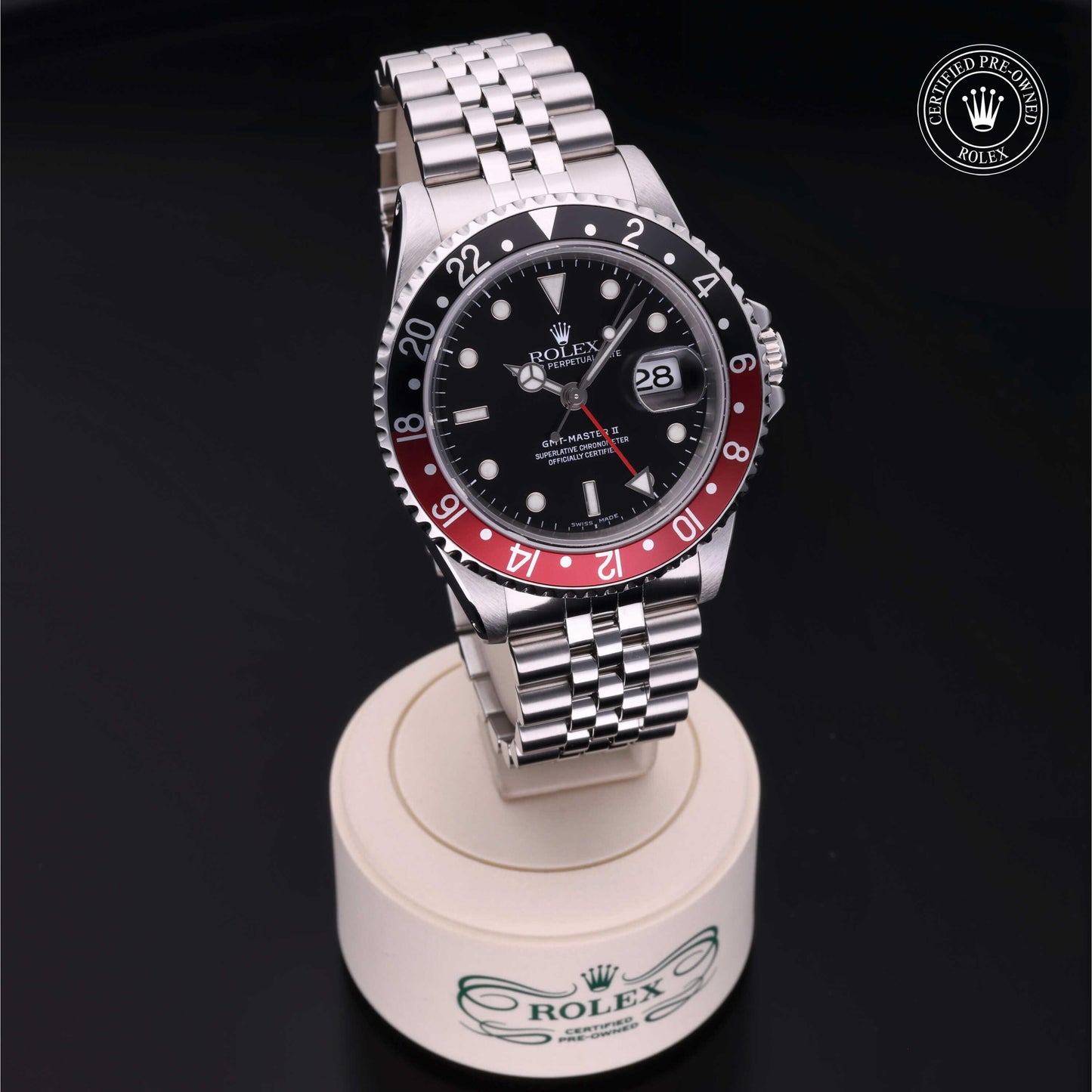 Rolex GMT-Master II with Jubilee bracelet, red and black bezel and black dial on a presentation stand against a black background.