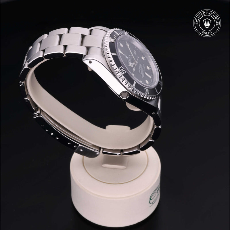 Rolex Sea-Dweller watch with a steel Oyster bracelet and black dial on cream stand with a black background.Sea-Dweller