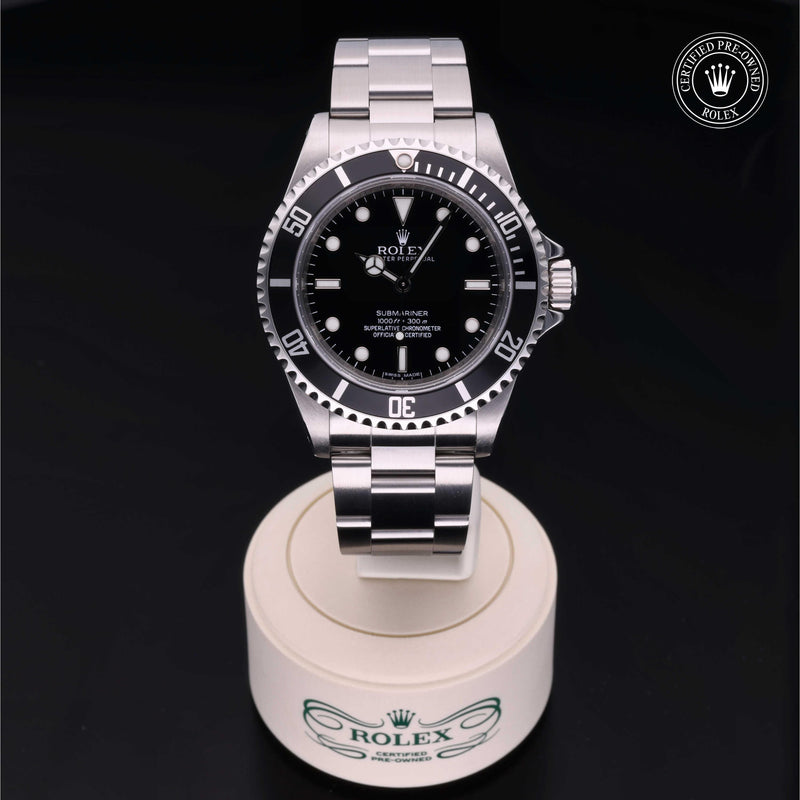 Rolex Submariner with steel Oyster bracelet and black dial, on a cream presentation stand against a black background.Submariner