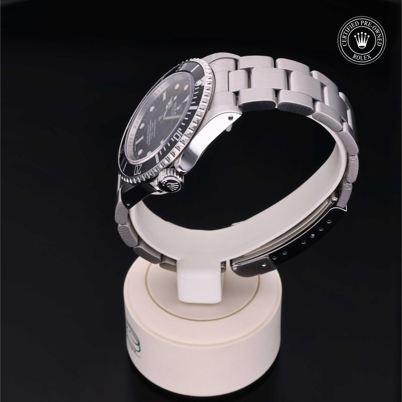 Rolex Submariner with steel Oyster bracelet and black dial, on a cream presentation stand against a black background.Submariner
