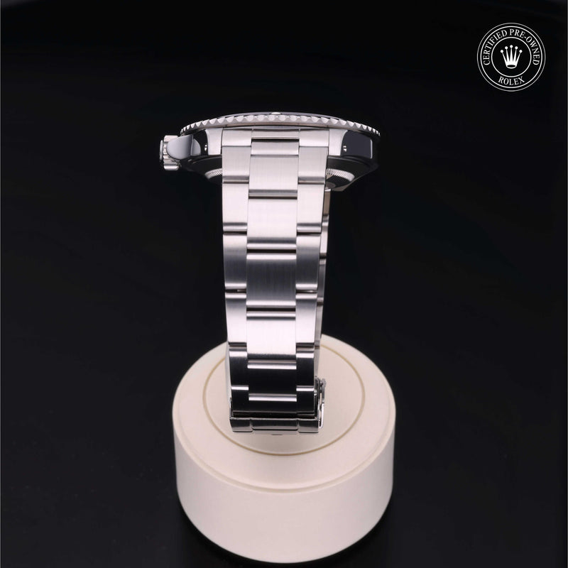 Rolex Submariner with steel Oyster bracelet and black dial, on a cream presentation stand against a black background.Submariner