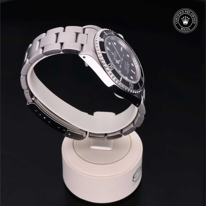 Rolex Submariner with steel Oyster bracelet and black dial, on a cream presentation stand against a black background.Submariner