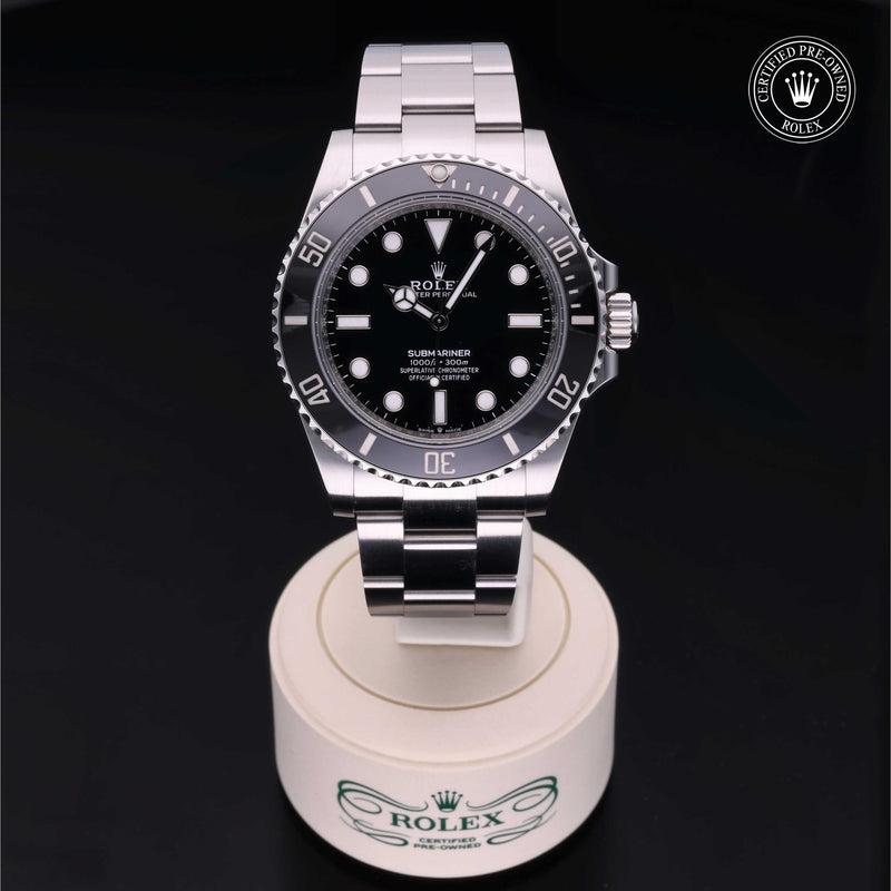 Rolex Submariner with steel Oyster bracelet and black dial, on a cream presentation stand against a black background.Submariner