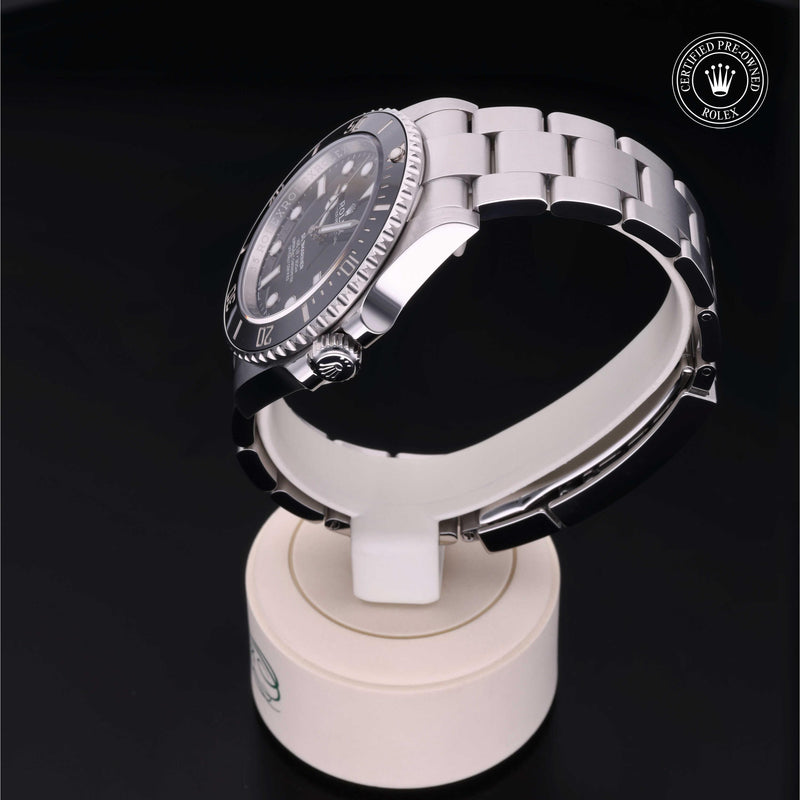 Rolex Submariner with steel Oyster bracelet and black dial, on a cream presentation stand against a black background.Submariner