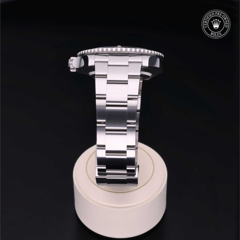 Rolex Submariner with steel Oyster bracelet and black dial, on a cream presentation stand against a black background.Submariner