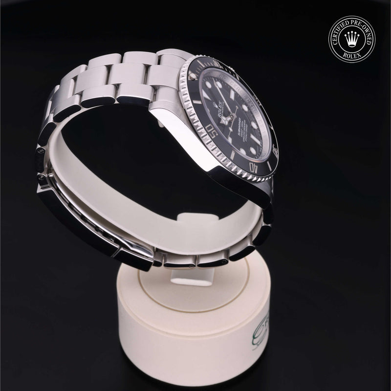Rolex Submariner with steel Oyster bracelet and black dial, on a cream presentation stand against a black background.Submariner