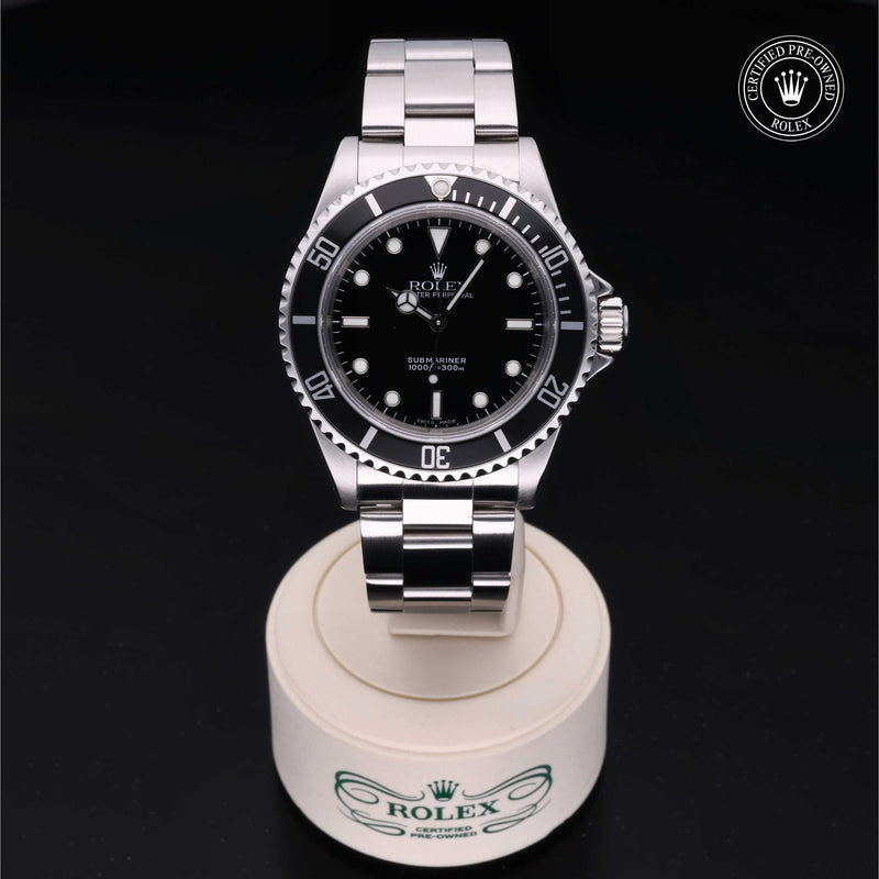Rolex Submariner watch with an Oyster bracelet and black dial on a white stand against a black background.Submariner
