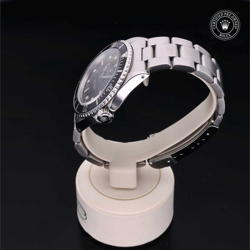 Rolex Submariner watch with an Oyster bracelet and black dial on a white stand against a black background.Submariner