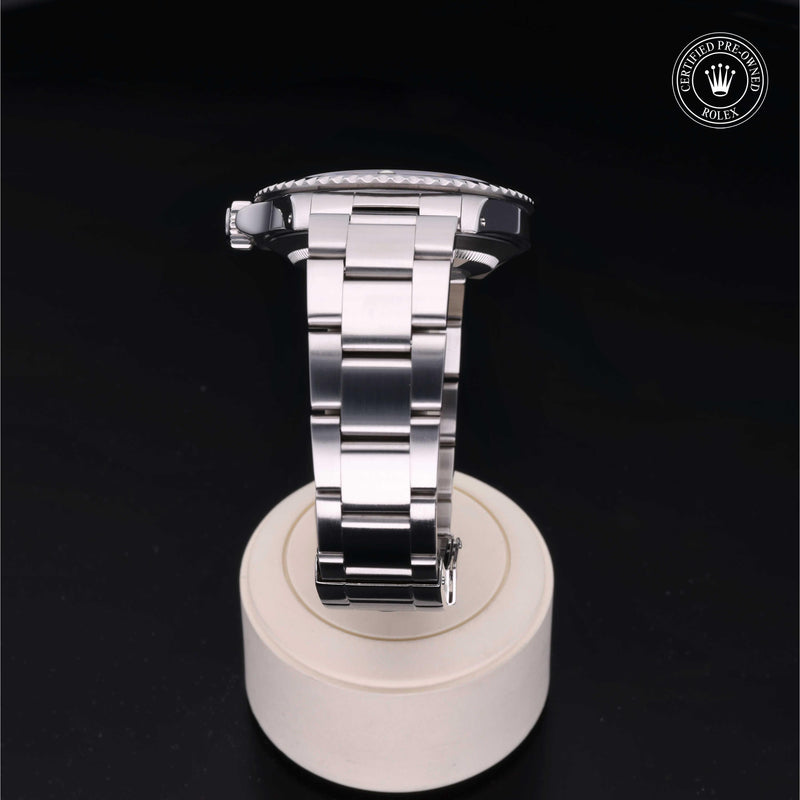 Rolex Submariner watch with an Oyster bracelet and black dial on a white stand against a black background.Submariner