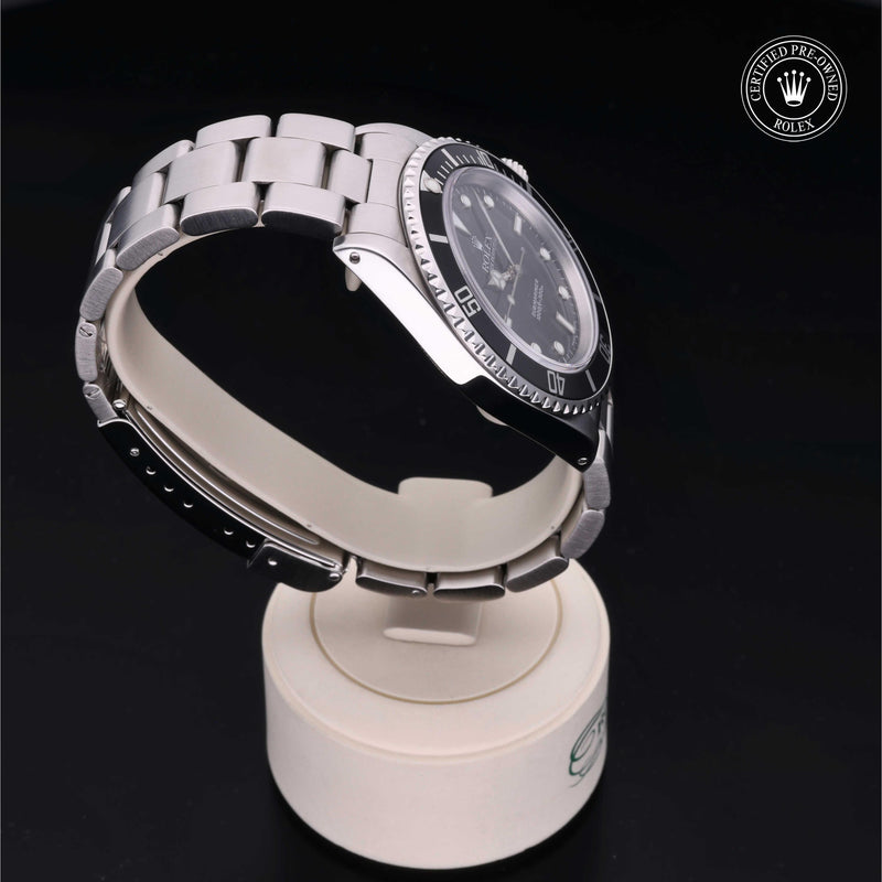 Rolex Submariner watch with an Oyster bracelet and black dial on a white stand against a black background.Submariner