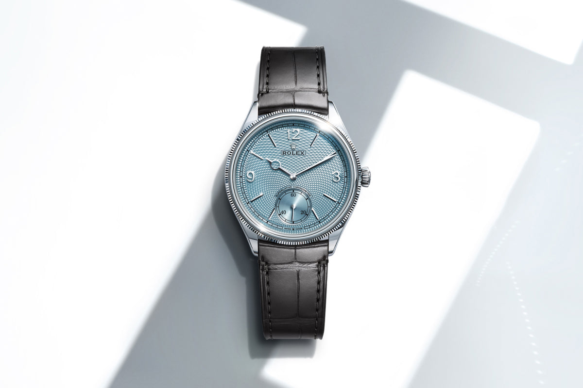 Rolex 1908 watch with a brown leather strap and blue dial on a reflective background.