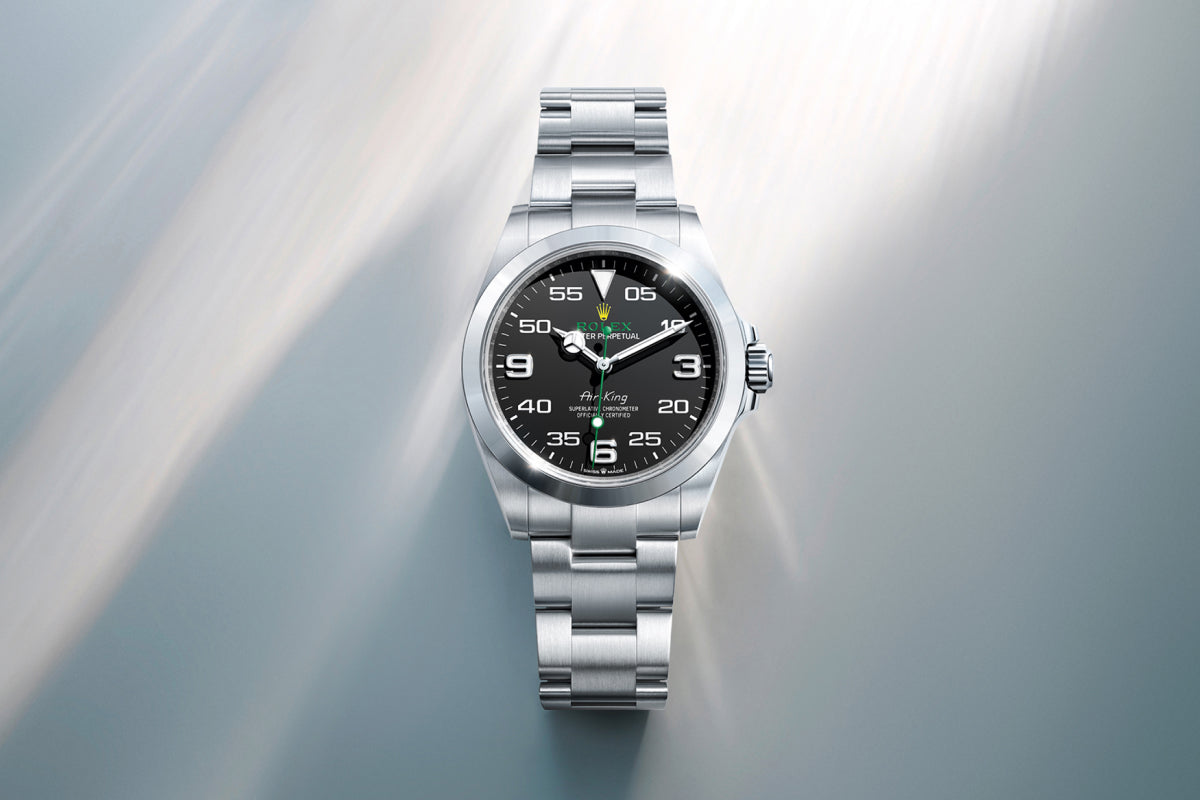Rolex Air-King watch with a steel bracelet and black dial on a reflective background.