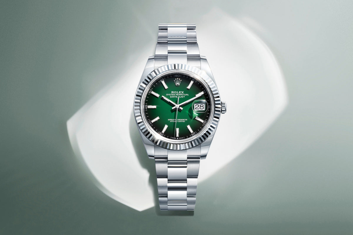 Rolex Datejust watch with a steel bracelet and green dial on a reflective background.