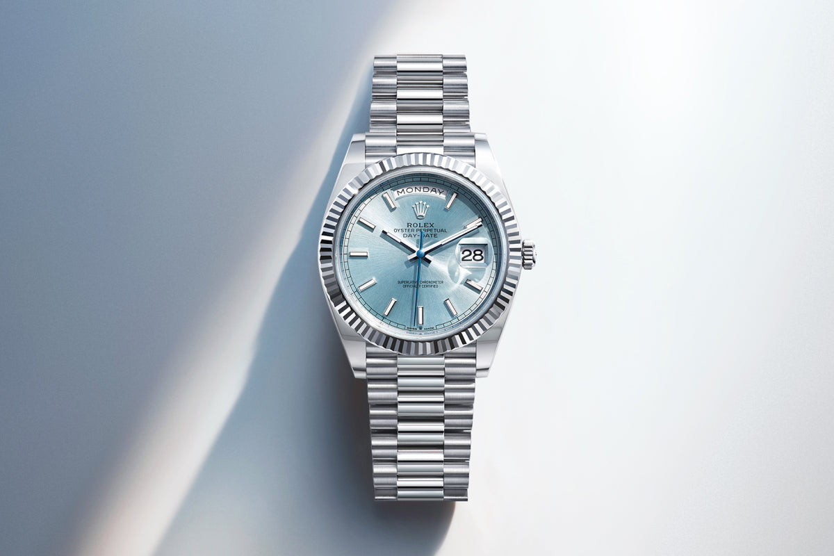 Rolex Day-Date watch with a platinum bracelet and blue dial on a reflective background.