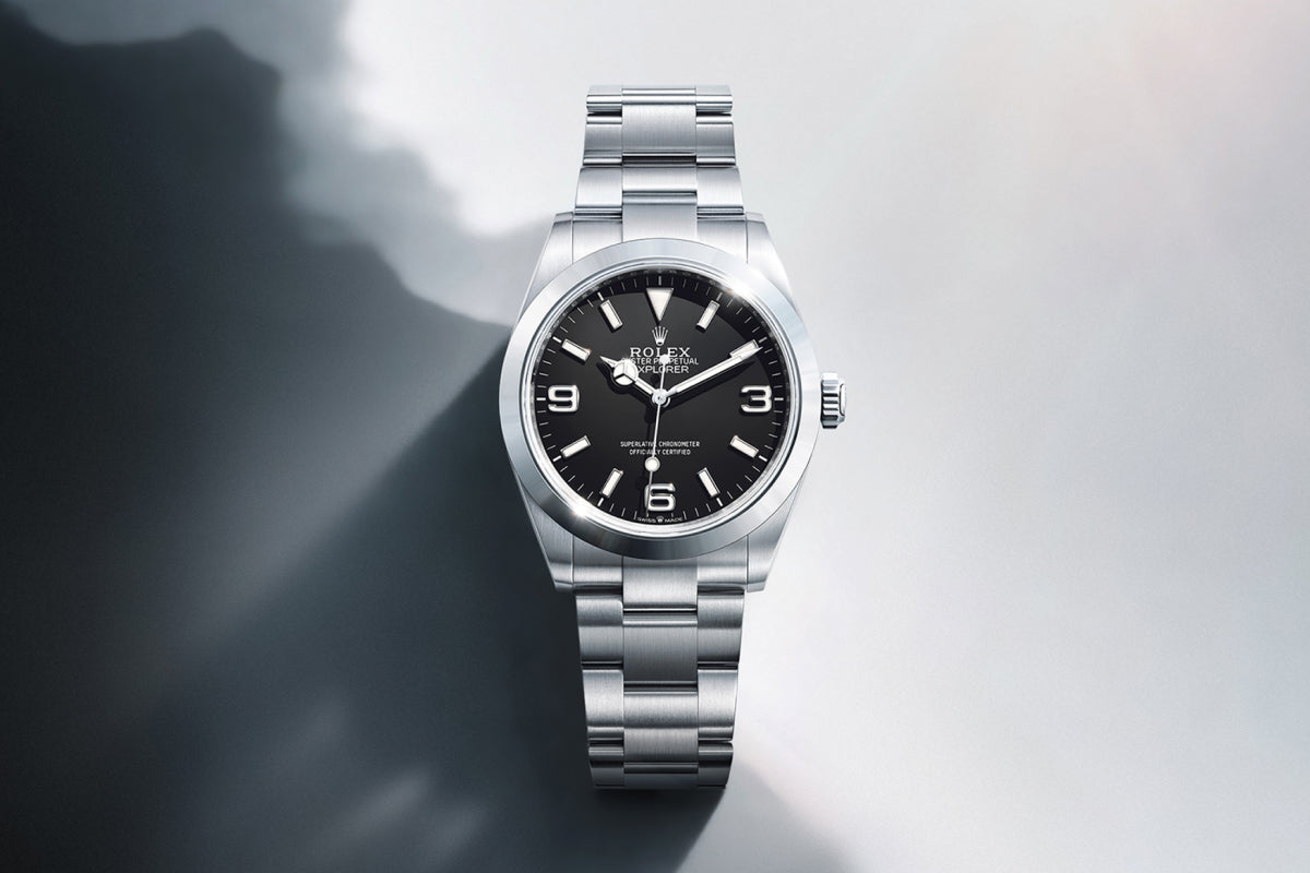 Rolex Explorer watch with a steel bracelet and black dial on a reflective background.