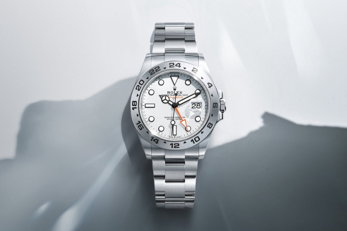 Rolex Explorer II watch with a steel bracelet and white dial on a reflective background.