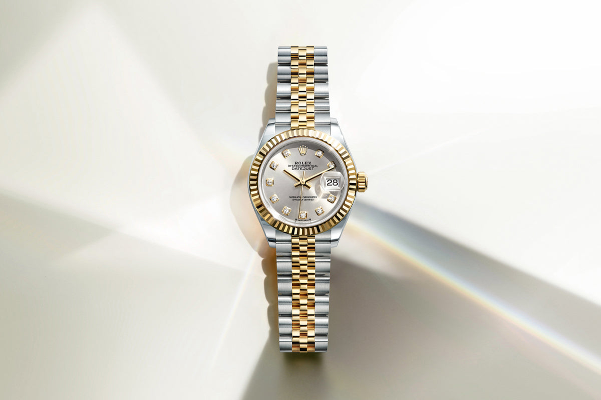 Rolex Lady-Datejust watch with a steel and yellow-gold bracelet, fluted bezel and silver dial on a reflective background.