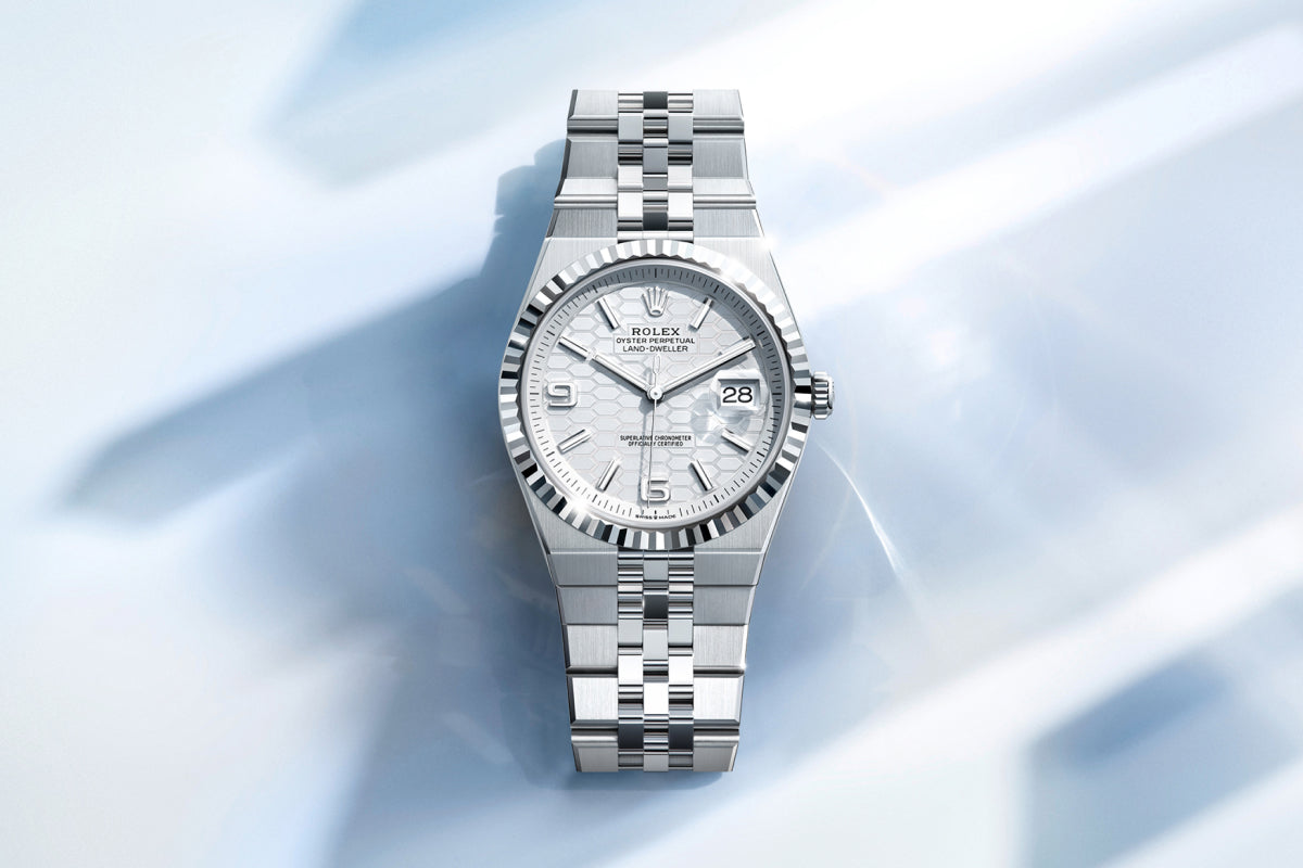 Rolex Land-Dweller watch with a platinum bracelet and white dial on a reflective background.
