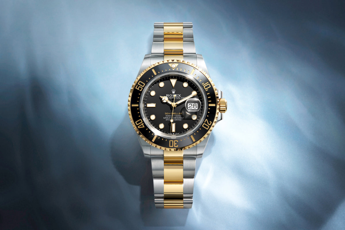 Rolex Sea-Dweller watch with a steel and yellow-gold bracelet and black dial on a reflective background.
