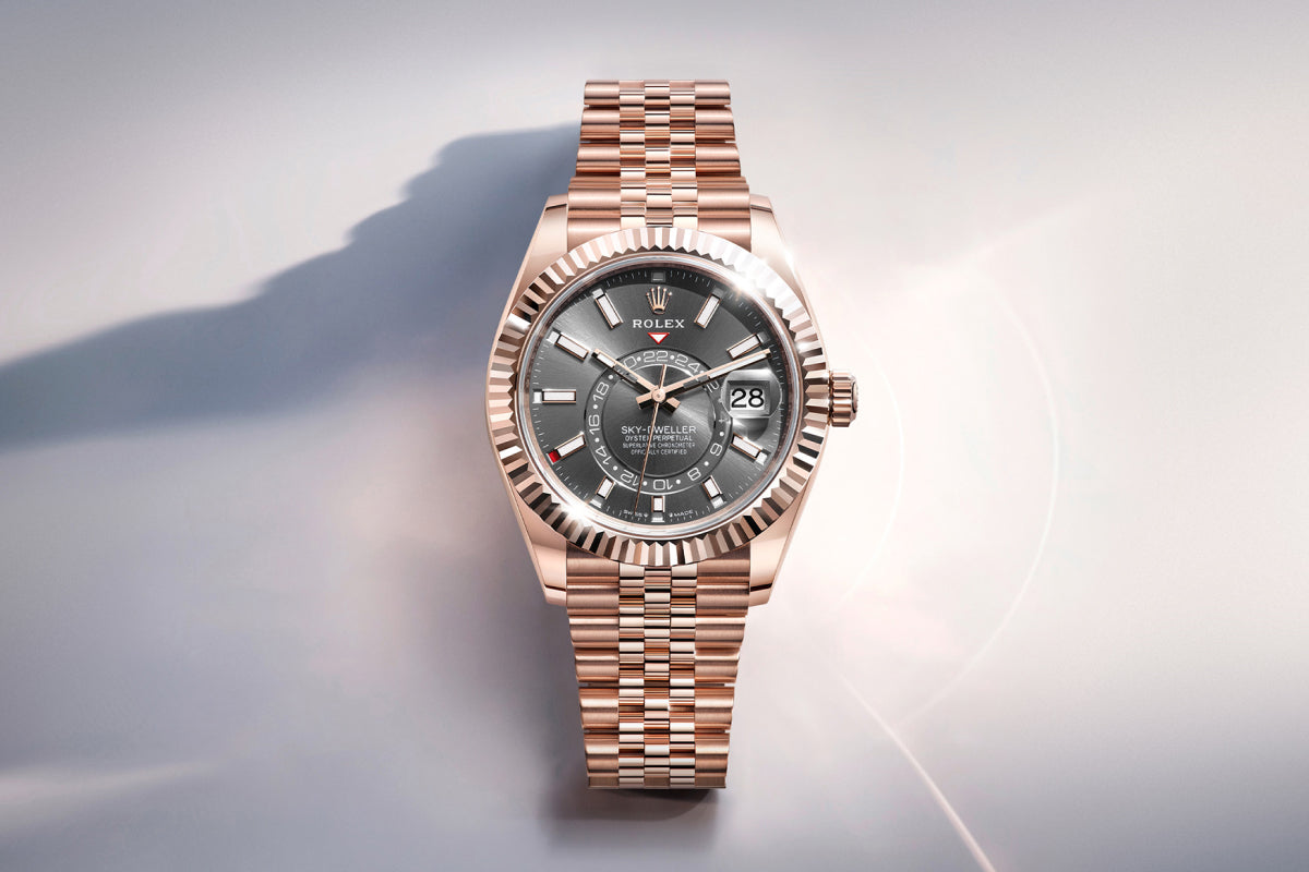 Rolex Sky-Dweller watch with a rose-gold bracelet, fluted bezel and slate dial on a reflective background.
