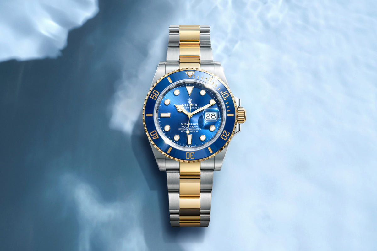 Rolex Submariner watch with a steel and yellow-gold bracelet and blue dial on a reflective background.