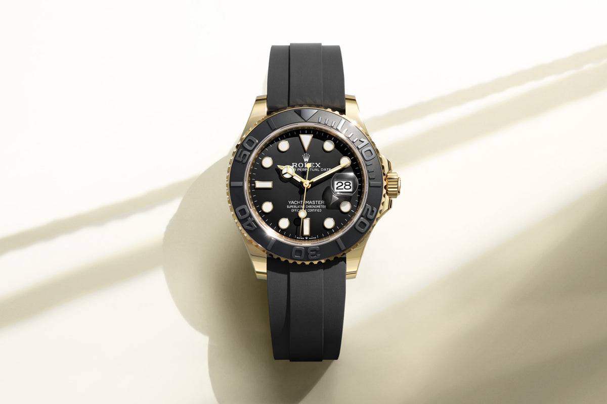 Rolex Yacht-Master watch on a black rubber strap with black dial on a reflective background.
