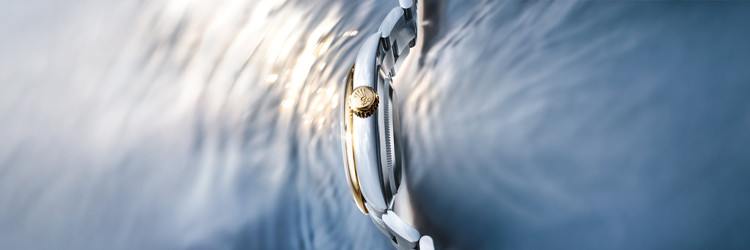 Side profile of Rolex watch with steel case and gold crown on a reflective background.