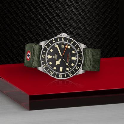 TUDOR Pelagos FXD GMT with 42mm titanium case, green fabric strap and black dial on a red board with black background.