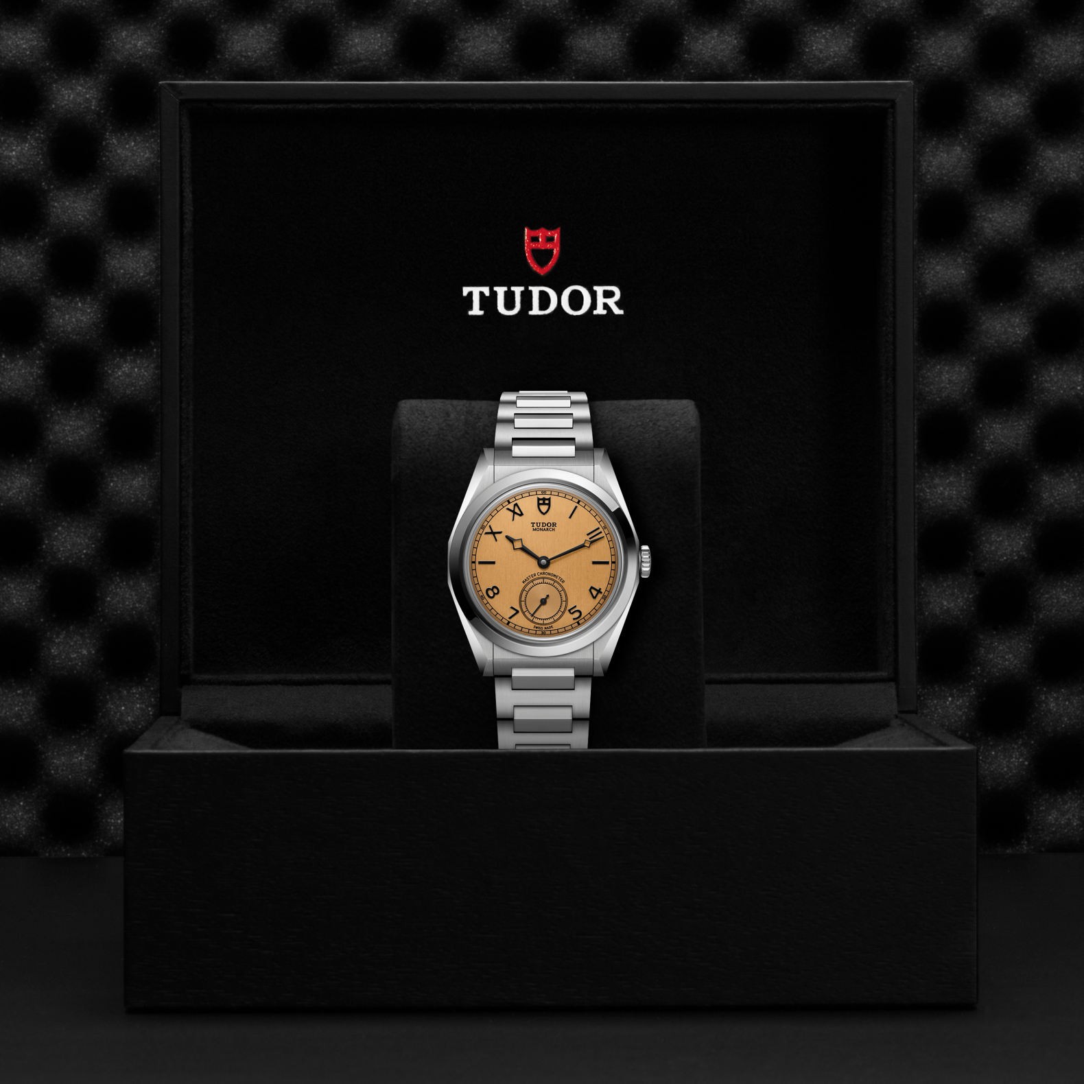 Tudor Monarch watch with steel bracelet and champagne dial in a black box against a black background.