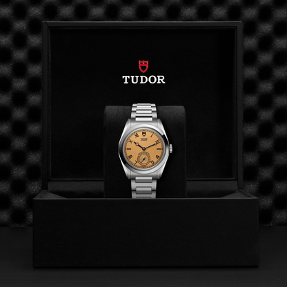 Tudor Monarch watch with steel bracelet and champagne dial in a black box against a black background.