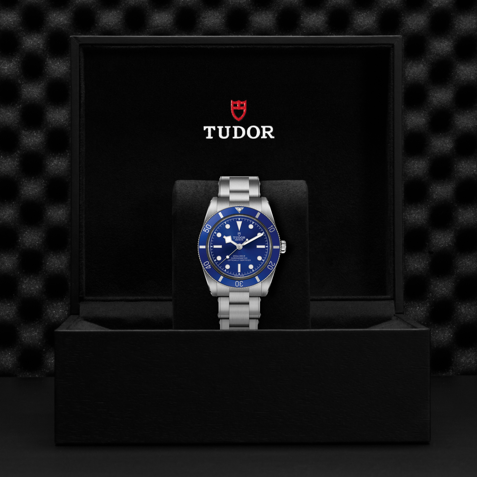 Tudor Black Bay 54 watch with a steel bracelet and blue dial in a black box against a black background.