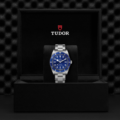 Tudor Black Bay 54 watch with a steel bracelet and blue dial in a black box against a black background.