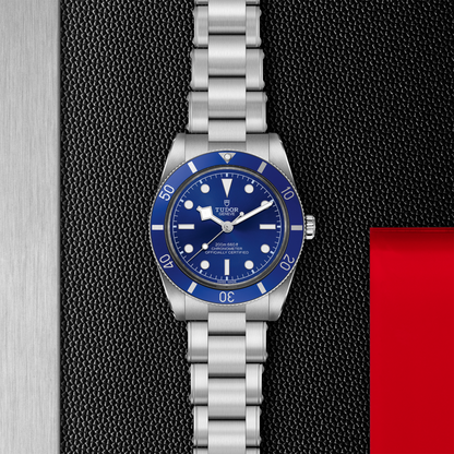 Tudor Black Bay 54 watch with a steel bracelet and blue dial on a black textured background.