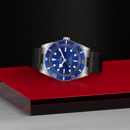 Tudor Black Bay 54 watch with a black rubber strap and blue dial on red platform against a black background.
