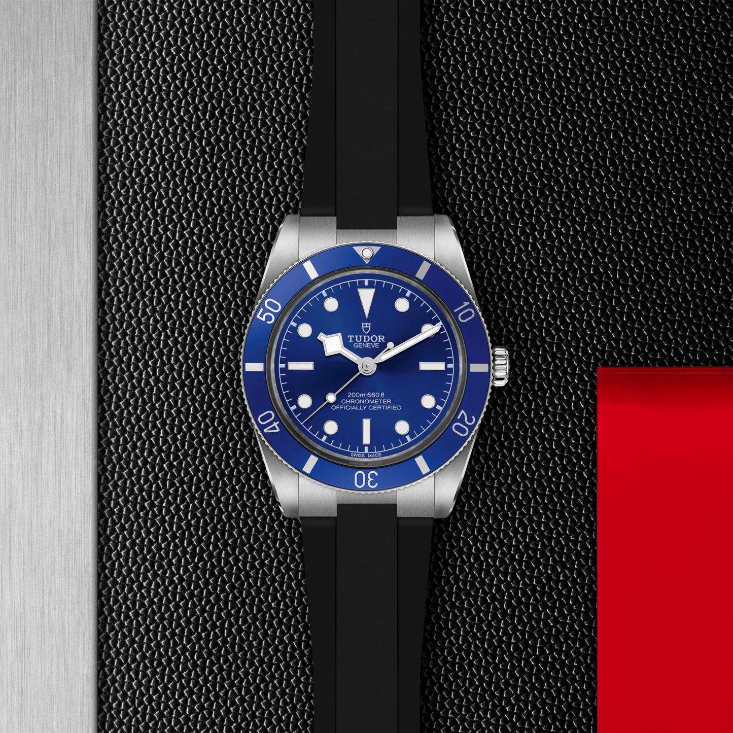 Tudor Black Bay 54 watch with a black rubber strap and blue dial on a black textured background.