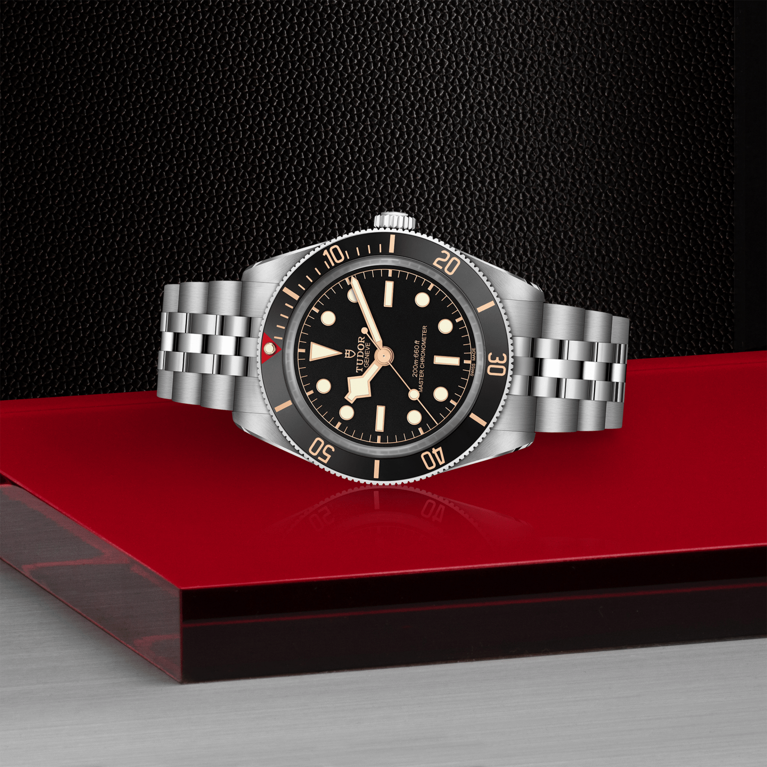 Tudor Black Bay 58 watch with a steel bracelet and black dial on red platform against a black background.