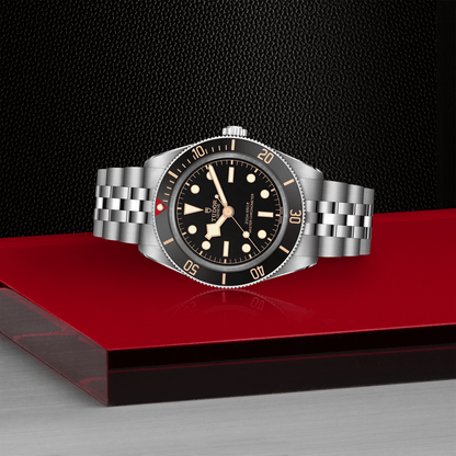 Tudor Black Bay 58 watch with a steel bracelet and black dial on red platform against a black background.