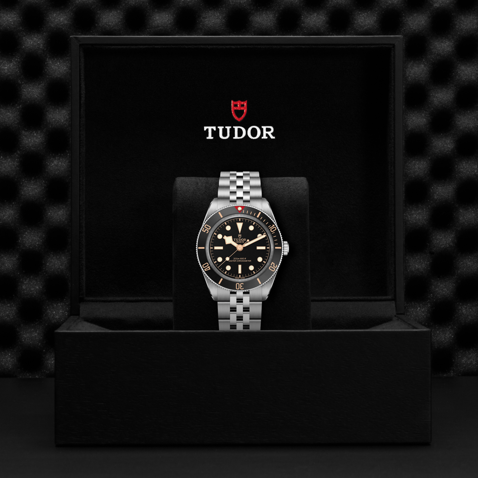 Tudor Black Bay 58 watch with a steel bracelet and black dial in a black box against a black background.