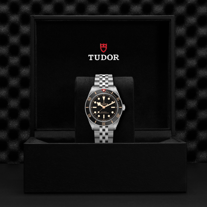 Tudor Black Bay 58 watch with a steel bracelet and black dial in a black box against a black background.