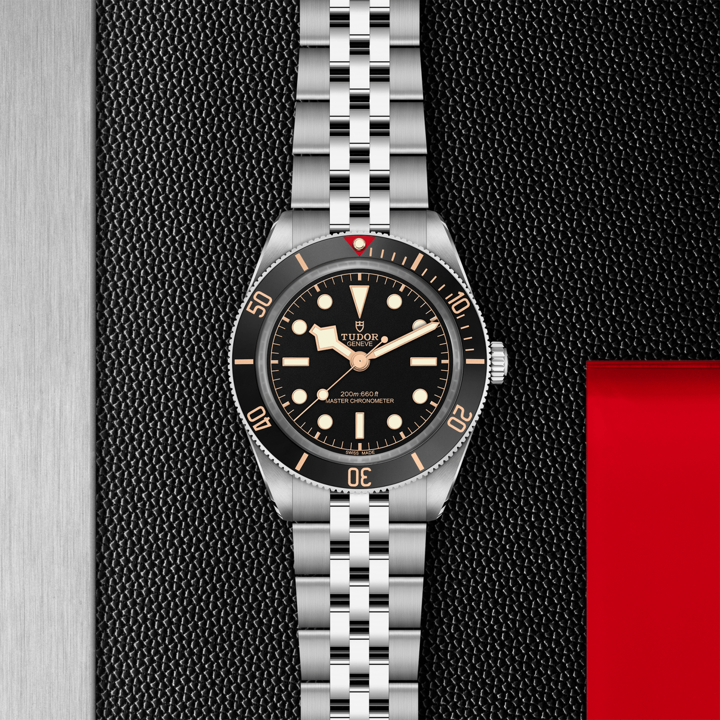 Tudor Black Bay 58 watch with a steel bracelet and black dial on a black textured background.