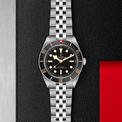 Tudor Black Bay 58 watch with a steel bracelet and black dial on a black textured background.