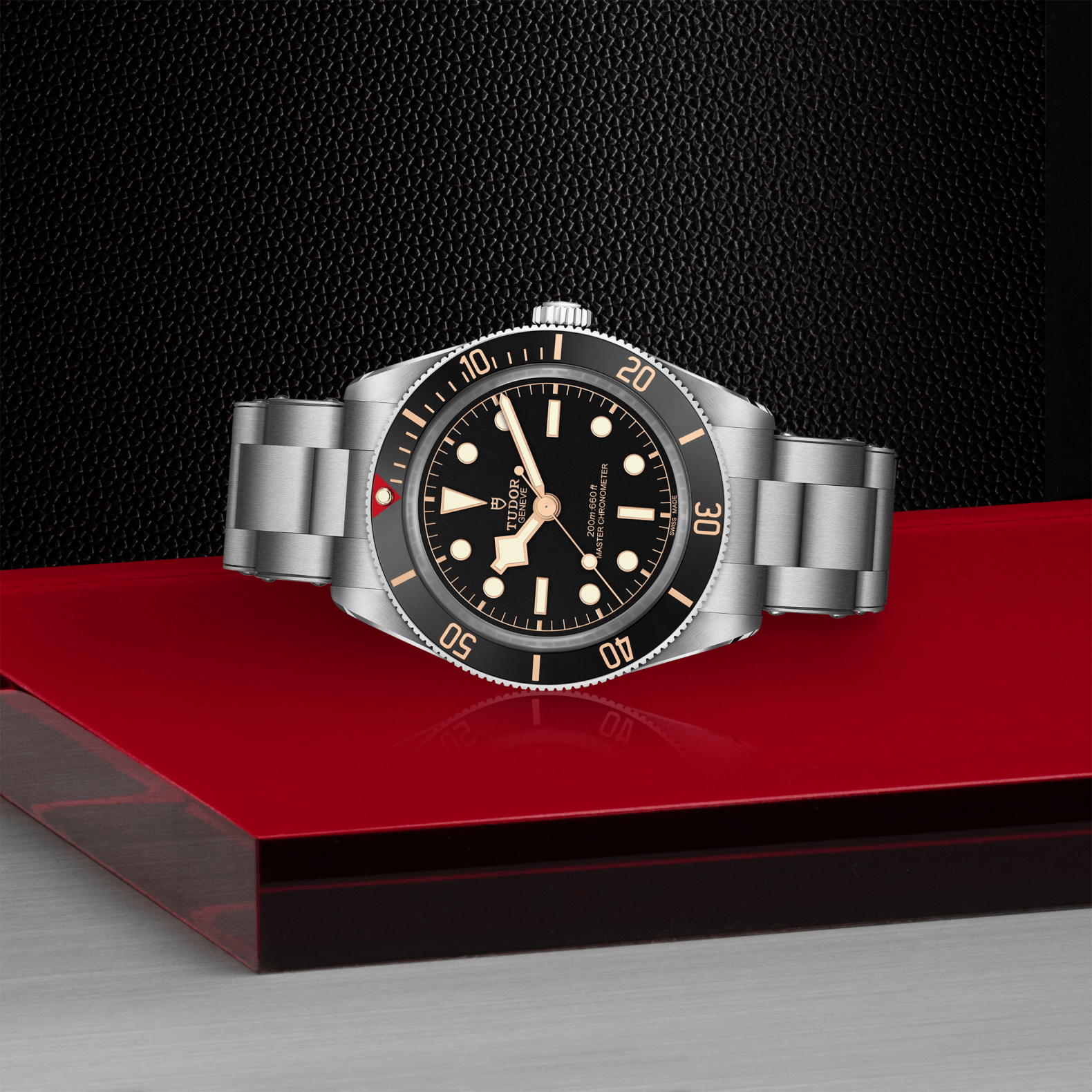 Tudor Black Bay 58 watch with a steel bracelet and black dial on red platform against a black background.