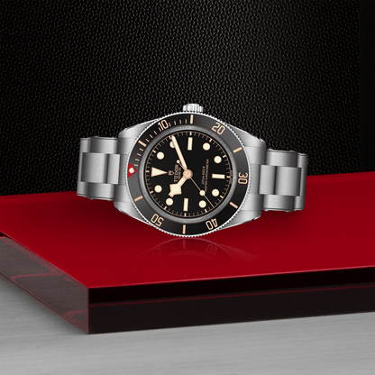 Tudor Black Bay 58 watch with a steel bracelet and black dial on red platform against a black background.