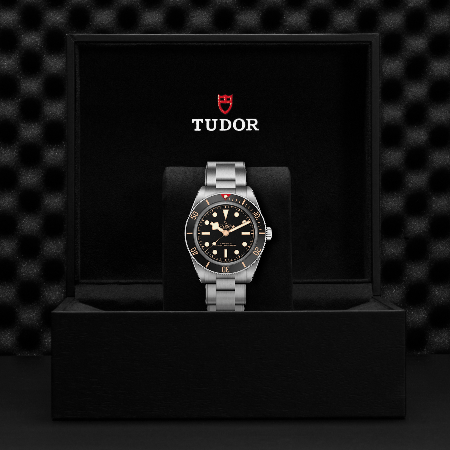 Tudor Black Bay 58 watch with a steel bracelet and black dial in a black box against a black background.