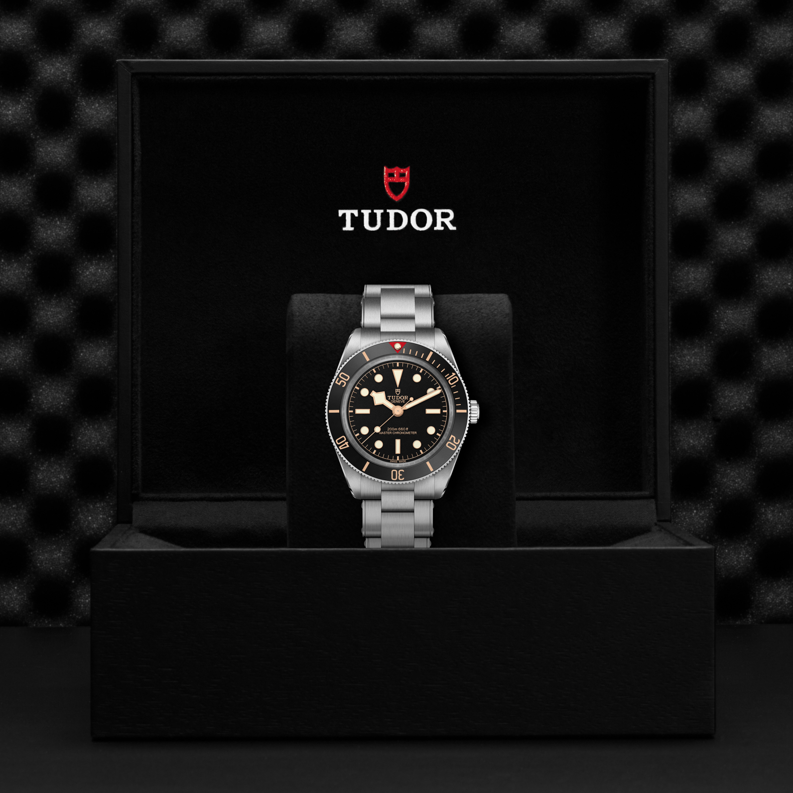 Tudor Black Bay 58 watch with a steel bracelet and black dial in a black box against a black background.
