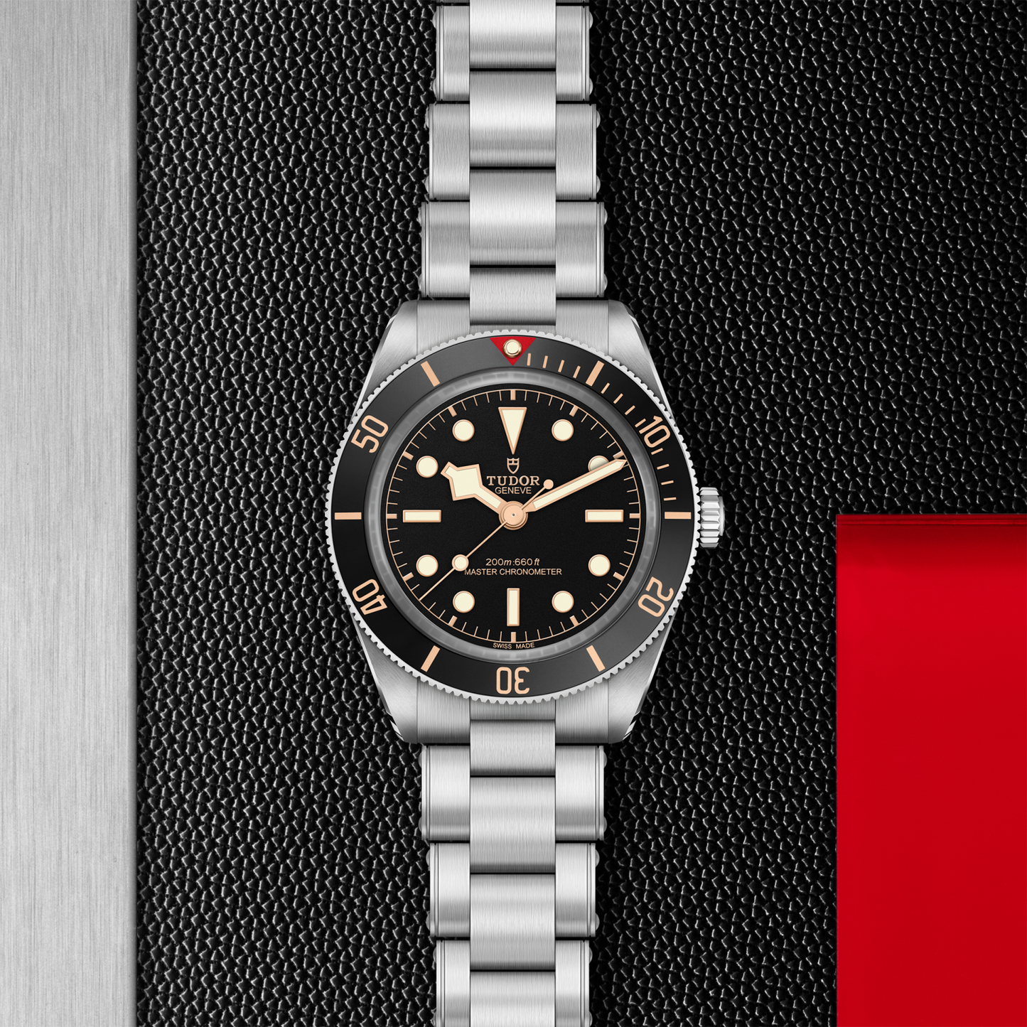 Tudor Black Bay 58 watch with a steel bracelet and black dial on a black textured background.