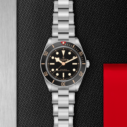 Tudor Black Bay 58 watch with a steel bracelet and black dial on a black textured background.